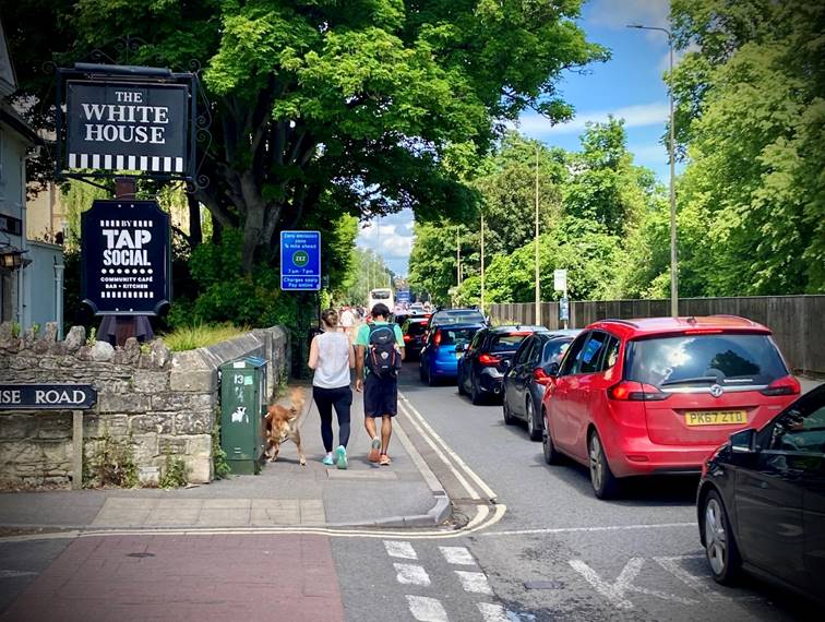 A group of people walking on a street with cars and trees

Description automatically generated